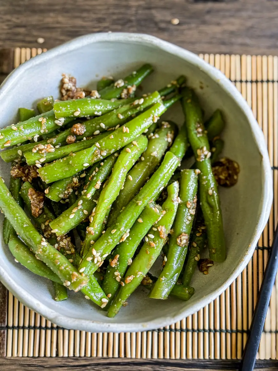 Close-up of Japanese gomaae green beans in a bowl, coated in nutty sesame dressing and sprinkled with sesame seeds.