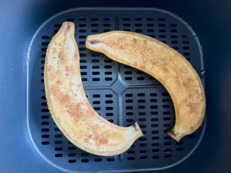 Two caramelized banana halves in an air fryer basket after cooking until golden and slightly crisp.