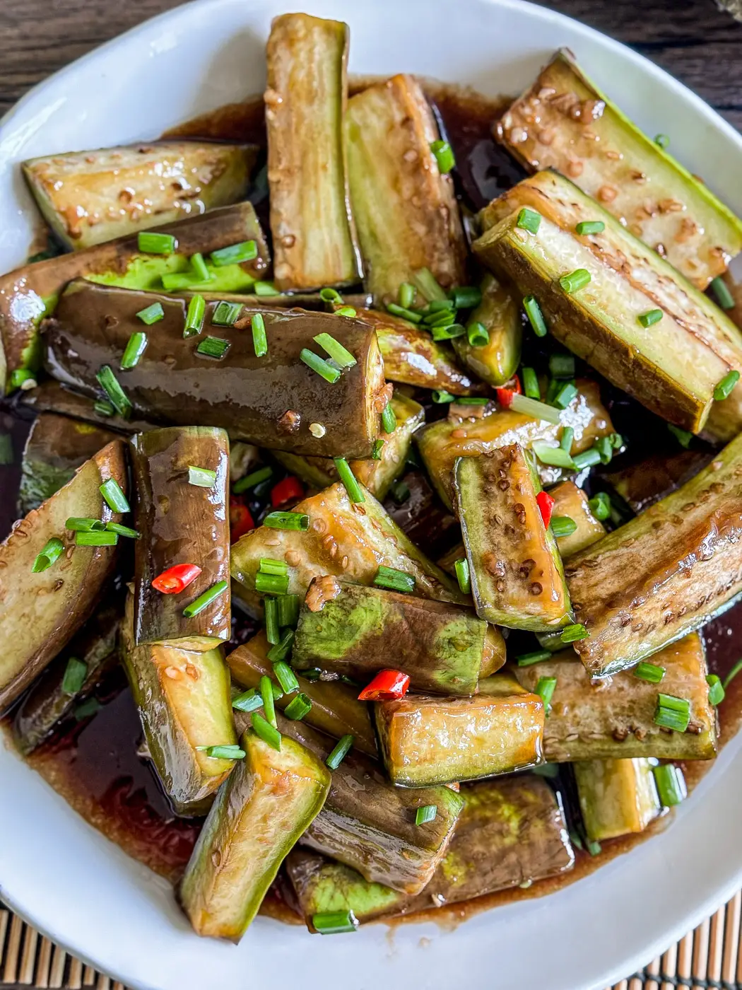 Asian eggplant stir-fry coated in a glossy savory sauce, garnished with fresh green onions and sliced red chilies.