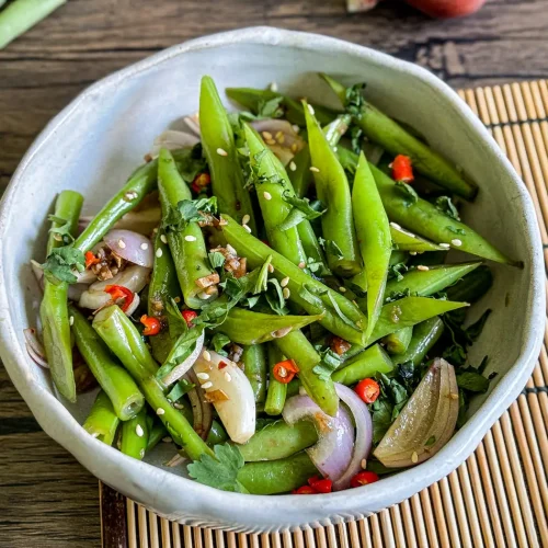 Asian green bean salad with fresh herbs, red chili, shallots, and sesame seeds served in a white bowl.