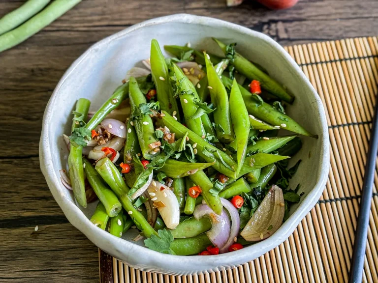 Asian green bean salad with fresh herbs, red chili, shallots, and sesame seeds served in a white bowl.