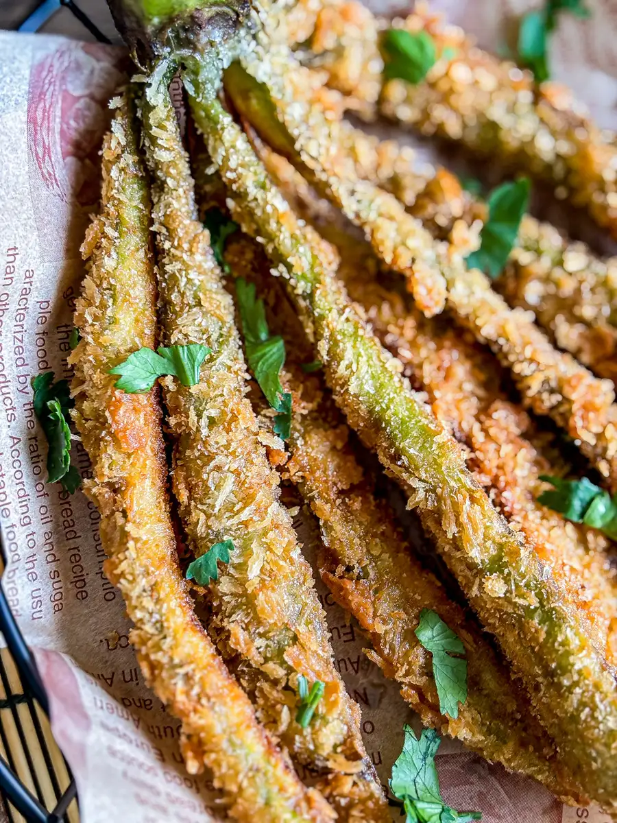 Close-up of crispy deep-fried whole eggplant strips coated in golden panko breadcrumbs and topped with fresh herbs.