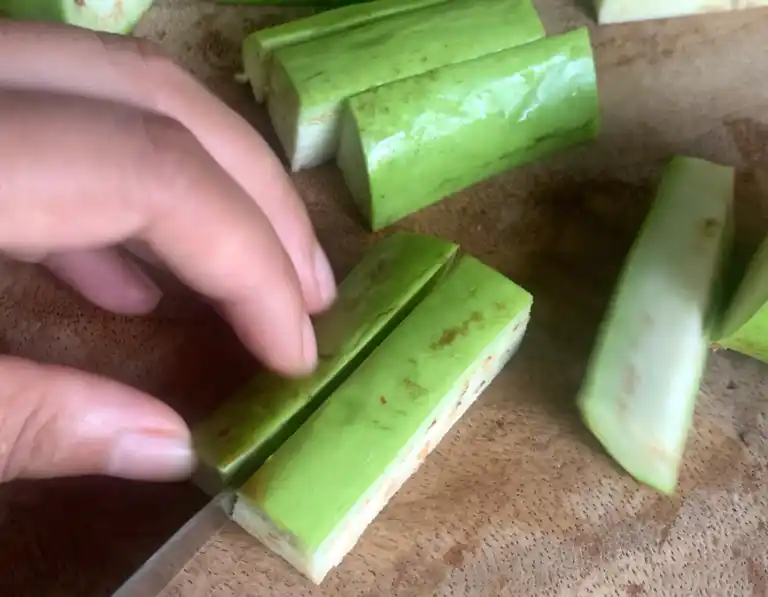 Cutting Chinese eggplant into thick batons on a wooden board.