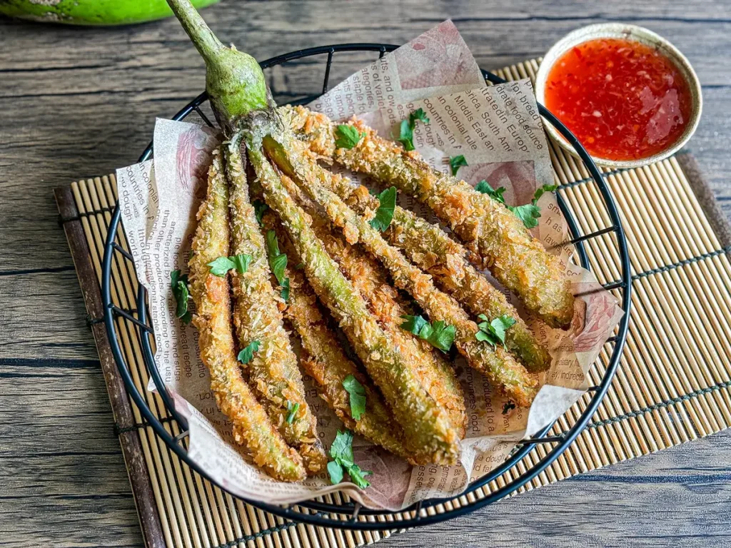deep-fried eggplant served with sweet chili dipping sauce on the side, presented on a bamboo mat.