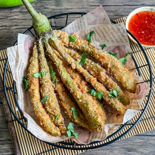 deep-fried eggplant served with sweet chili dipping sauce on the side, presented on a bamboo mat.