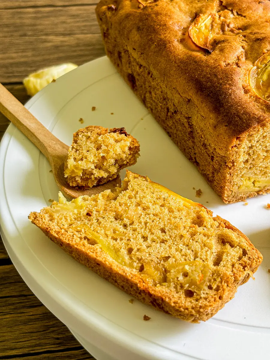 Slice of homemade durian cake on a white plate with wooden spoon and loaf in the background – durian fruit dessert close-up.