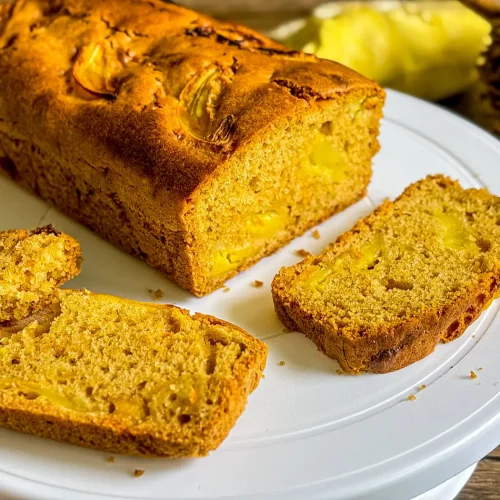 Sliced durian cake loaf on white cake stand with visible durian chunks and a wooden spoon holding a soft bite.