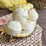 Homemade durian ice cream served in a half durian shell on a woven mat, with wooden spoon on the side.