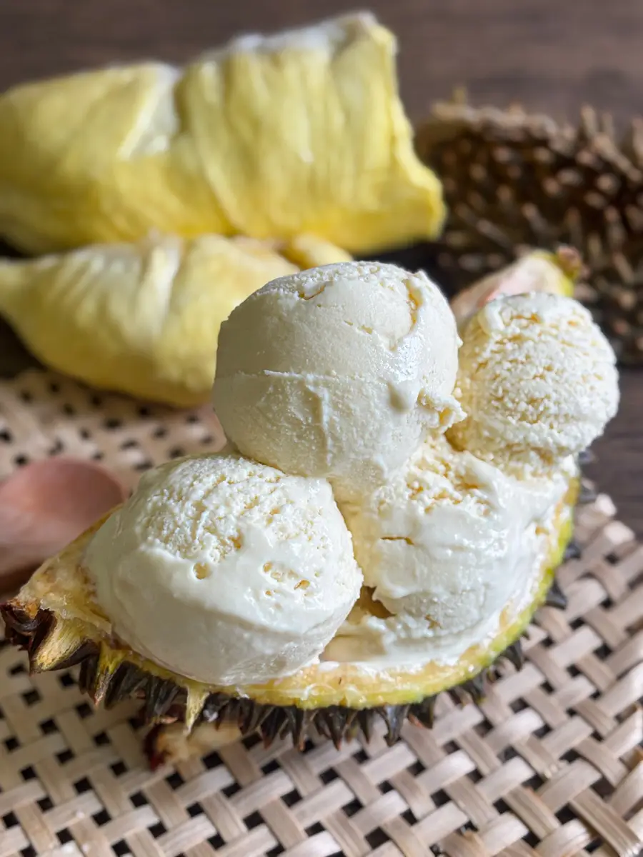 Scoops of creamy durian ice cream in a durian shell with fresh fruit in the background.