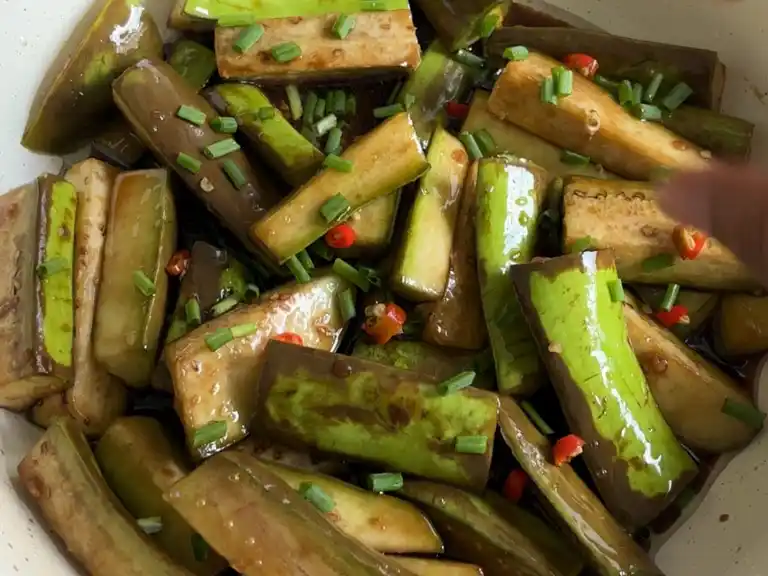 Cooked Chinese eggplant stir-fry garnished with chopped chilies and scallions.