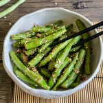 Japanese green bean salad gomaae served in a white bowl with chopsticks on the side, topped with sesame seeds.