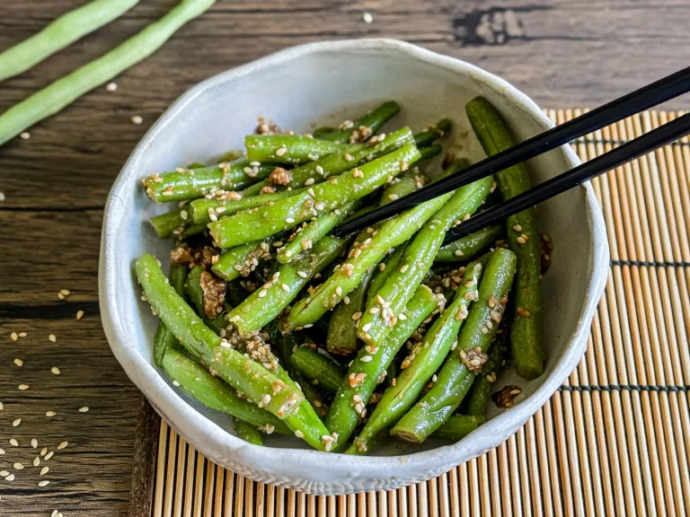 Japanese green bean salad gomaae served in a white bowl with chopsticks on the side, topped with sesame seeds.