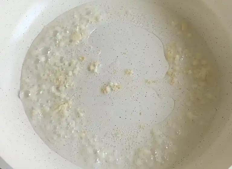 Garlic sizzling in hot oil in a white nonstick pan.