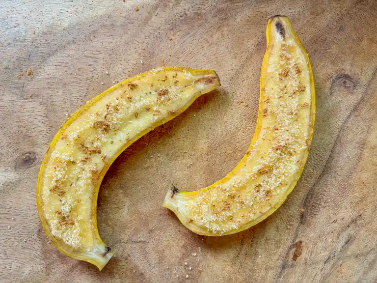 Two banana halves sprinkled with sugar and cinnamon on a wooden board.