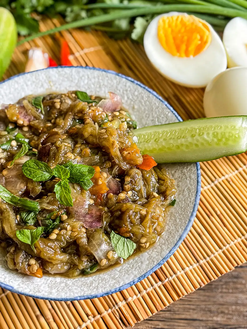 Thai eggplant dip with mint, cucumber, and hard-boiled eggs on the side, served in a white ceramic bowl.