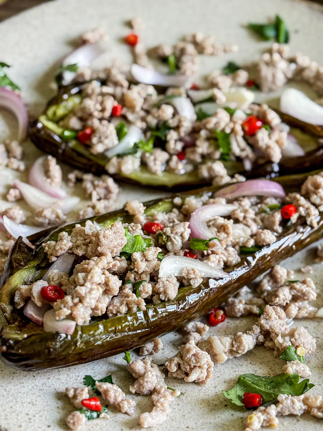 Close-up of Thai grilled eggplant salad topped with ground pork, fresh red chilies, shallots, and herbs.