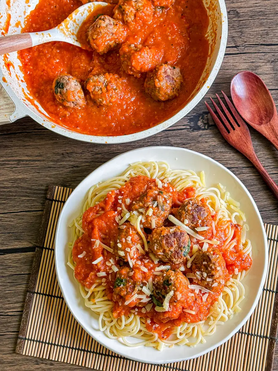 Thai meatball spaghetti topped with meatballs in a rich red tomato sauce, served on a white plate with grated cheese.