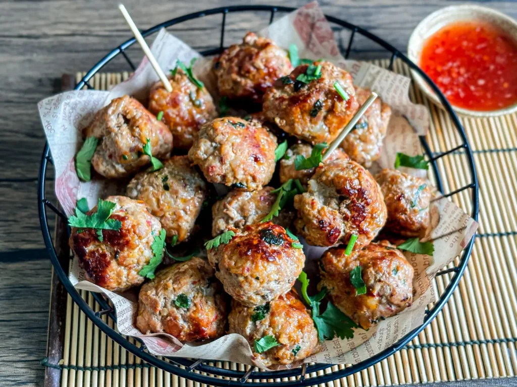 Thai meatballs garnished with cilantro, served with a side of sweet chili sauce.