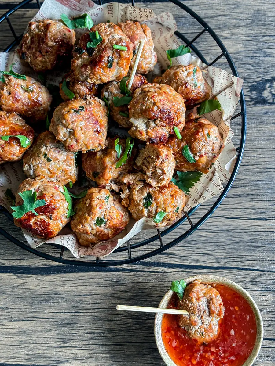 Thai pork meatballs with cilantro, served in a basket with sweet chili sauce on the side.