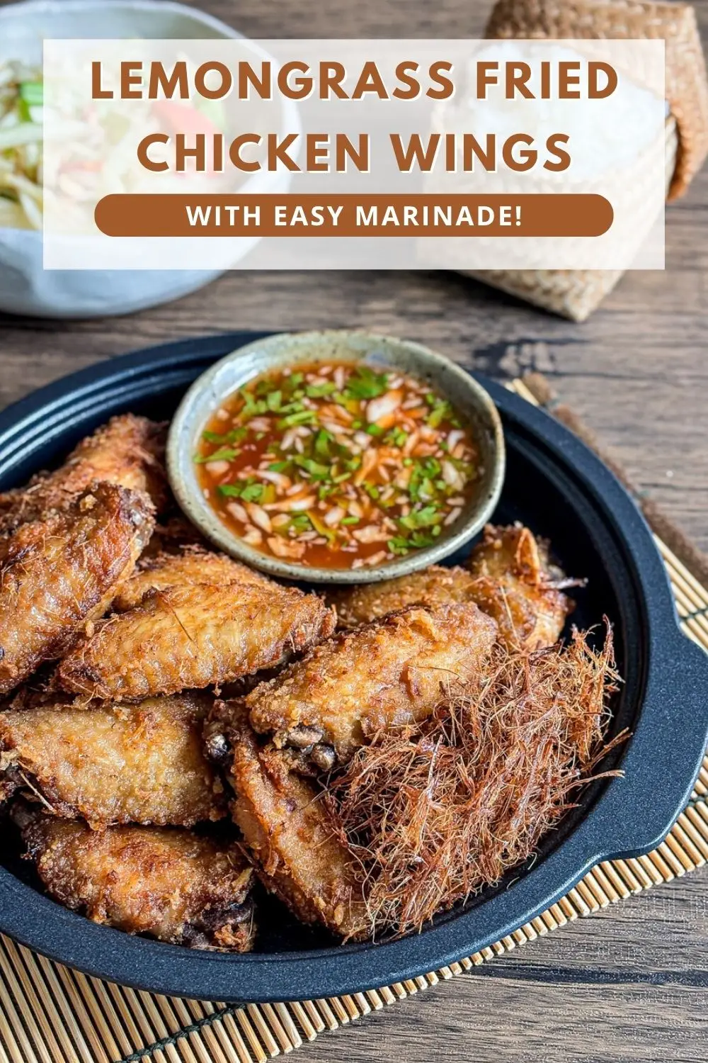 Thai lemongrass fried chicken wings served with dipping sauce in a black dish, topped with crispy fried lemongrass.