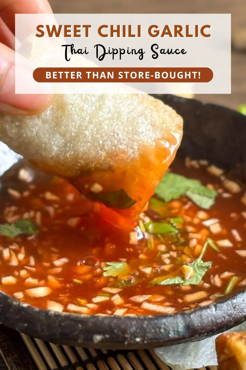 Thai sweet chili garlic dipping sauce with chopped garlic and herbs in a black bowl, served with crispy spring rolls.