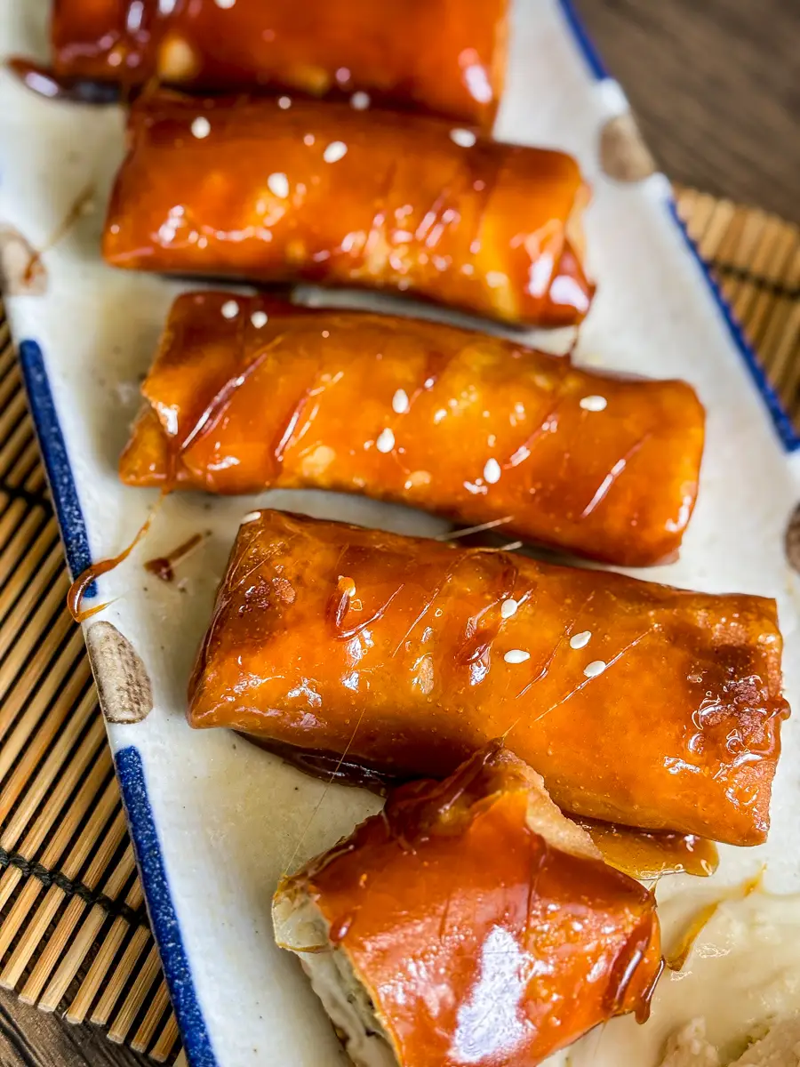 Top view of golden brown turon (banana lumpia with caramel) with sesame seeds and caramel glaze, with one piece cut open to show the banana filling.