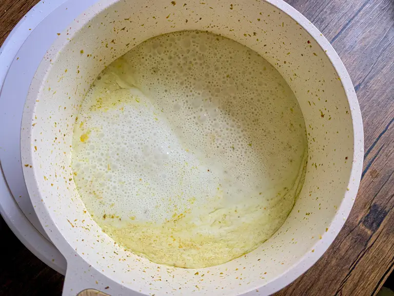 Coconut milk added to the fried curry paste in a white pot, gently bubbling.