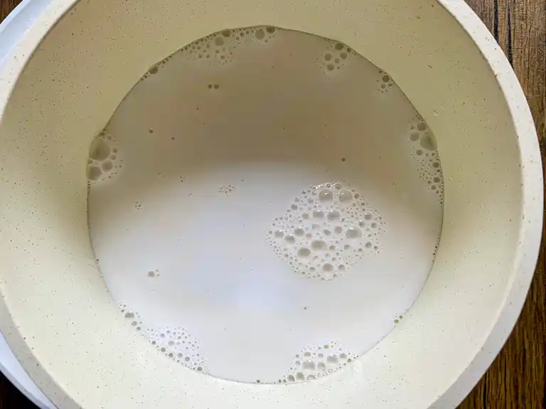 Full-fat coconut milk simmering in a white pot.