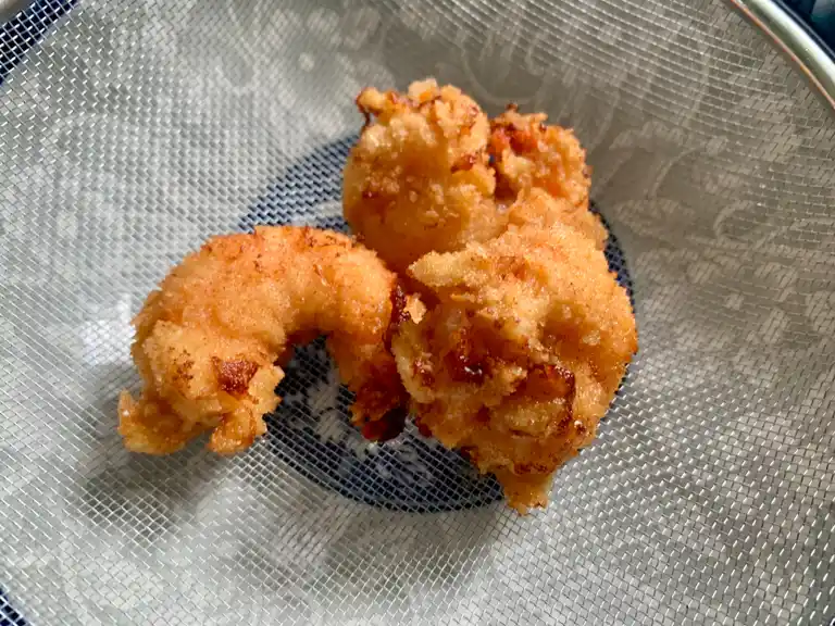 Golden crispy panko fried shrimp draining on a rack after frying.