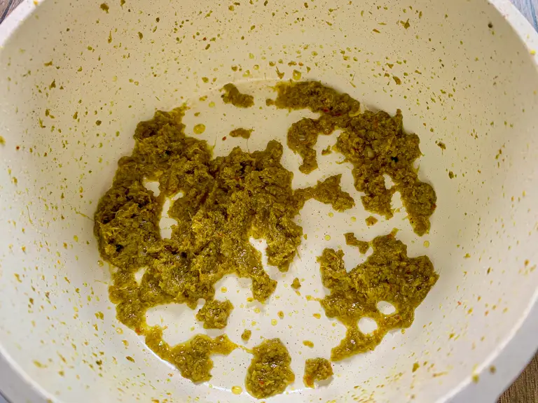 Green curry paste frying in a white pot until fragrant with oil starting to separate.