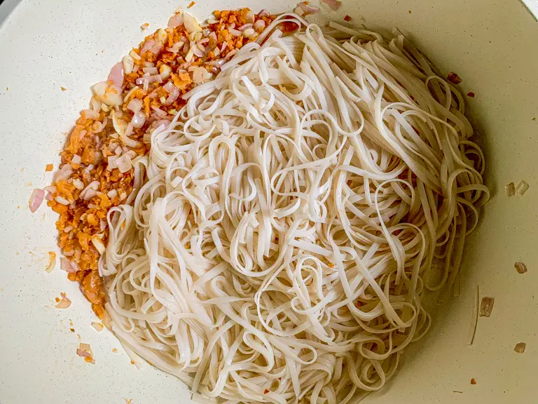 Soaked rice noodles added to stir-fried aromatics in the pan.