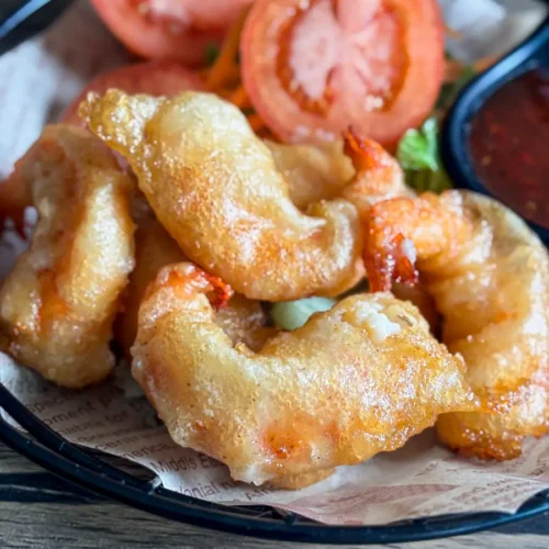 Golden crispy panko fried shrimp served with fresh tomato slices on a plate.