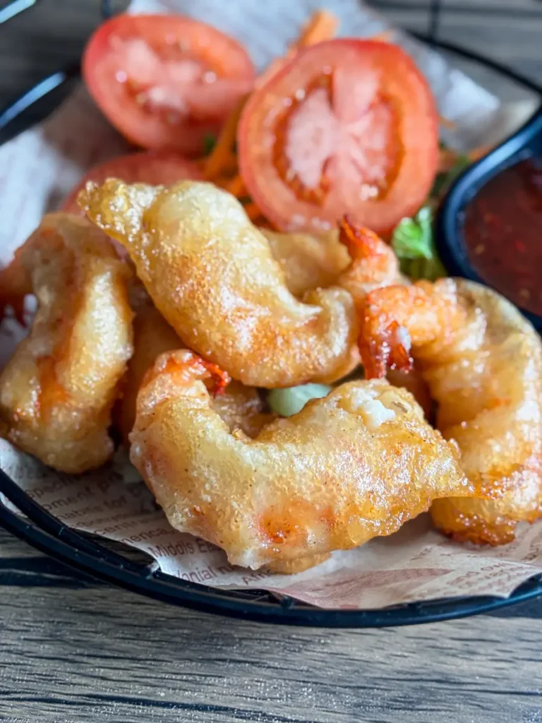 Golden crispy panko fried shrimp served with fresh tomato slices on a plate.