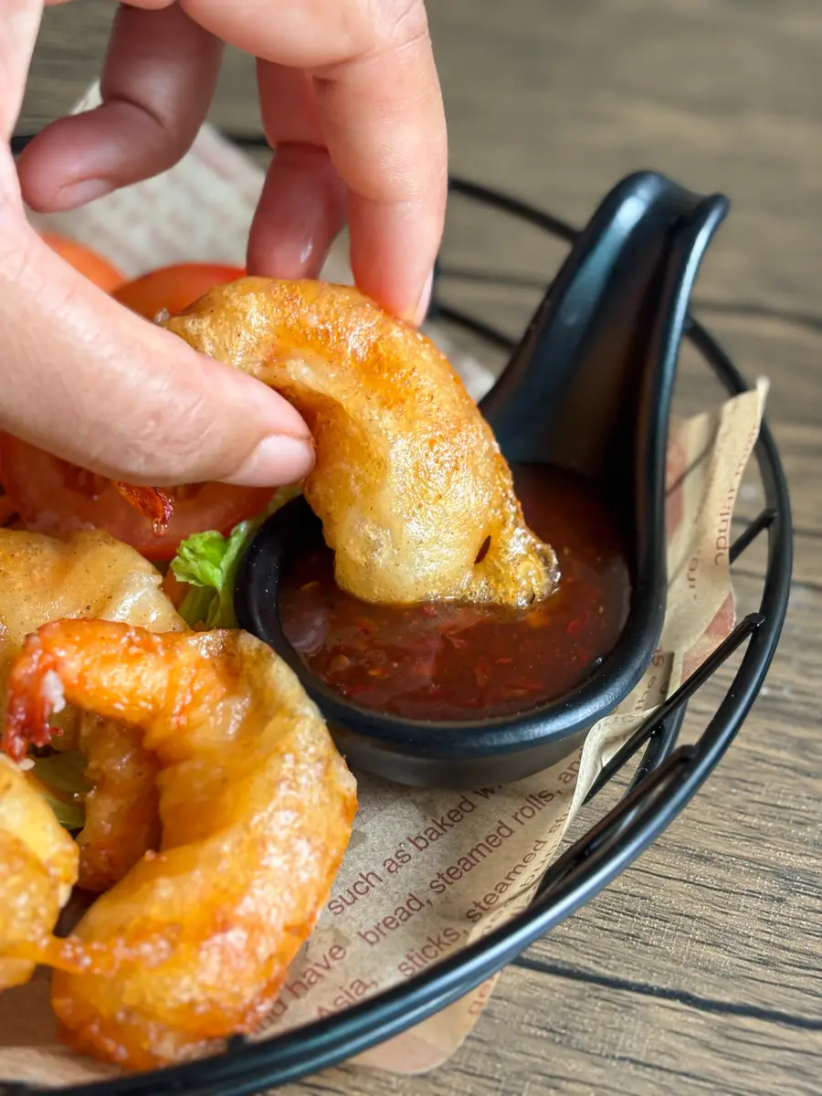 Hand dipping crispy panko fried shrimp into sweet chili dipping sauce.