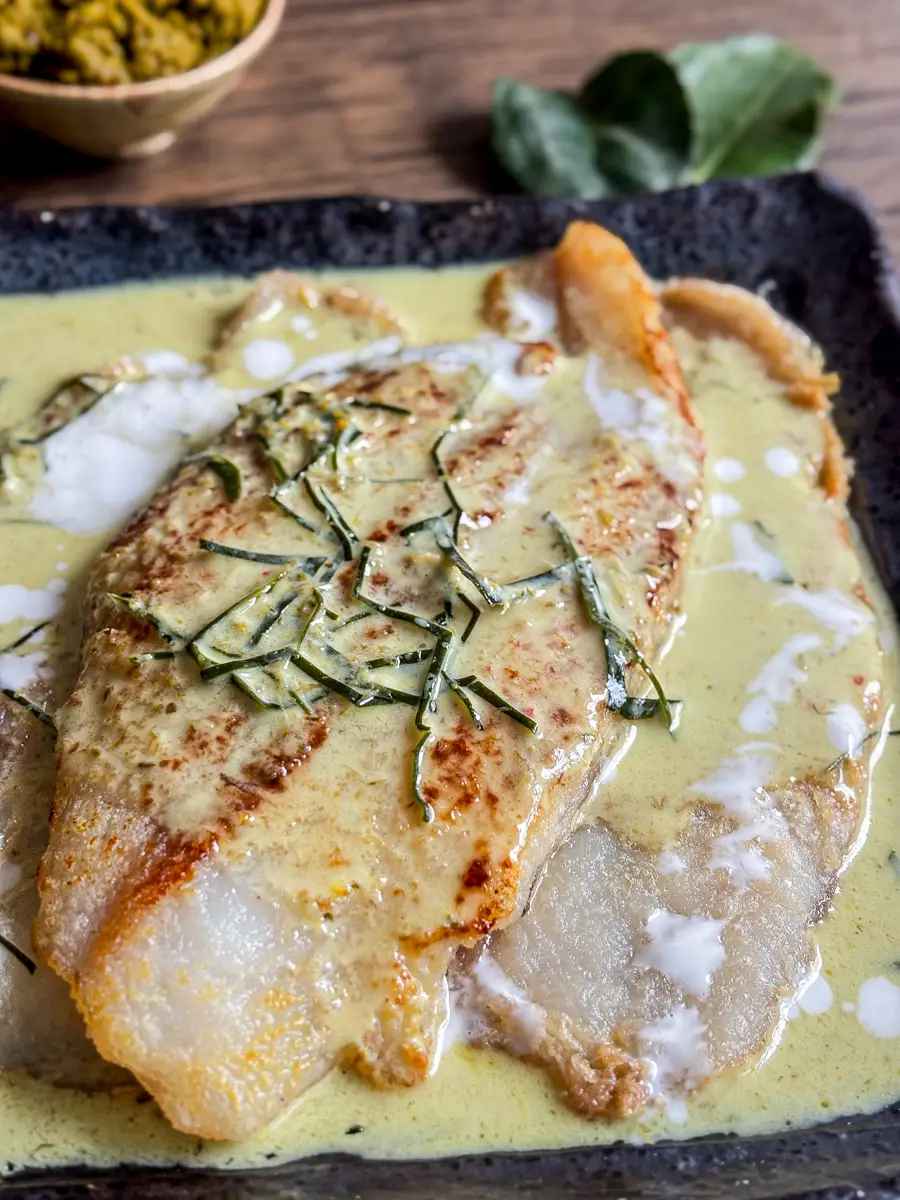 Thai green fish curry with pan-fried fish and sliced kaffir lime leaves in a black plate.
