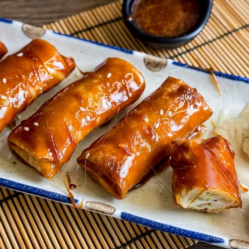 Crispy fried banana lumpia (turon) topped with sticky caramel sauce, served with a scoop of vanilla ice cream on a ceramic plate.