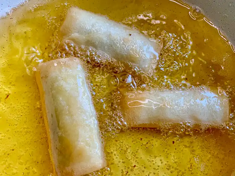 Banana lumpia being deep-fried in hot oil until golden and crispy.