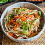 Asian bean sprout salad with julienned carrots, cucumber, cilantro, and sesame soy dressing in a ceramic bowl.