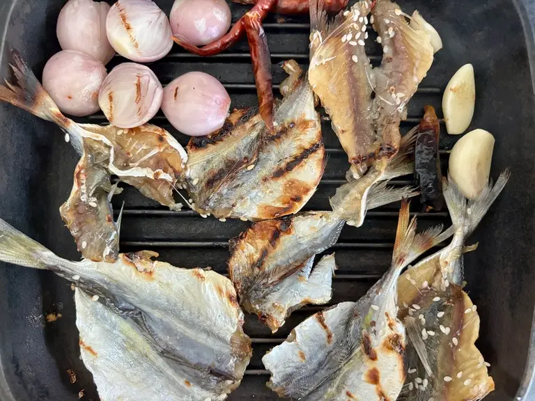 Grilled dried fish, garlic, shallots, and chilies on a grill pan.