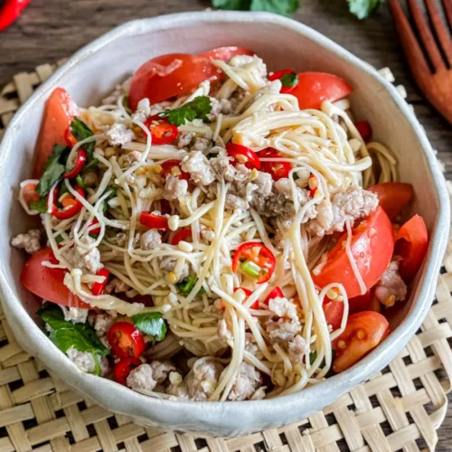 Asian enoki mushroom salad with red chili, tomato wedges, coriander, and ground pork in a ceramic bowl.