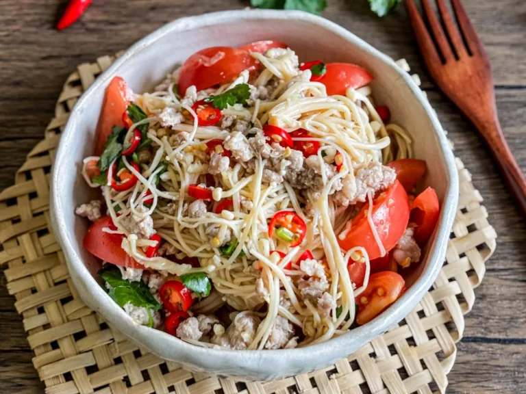 Asian enoki mushroom salad with red chili, tomato wedges, coriander, and ground pork in a ceramic bowl.