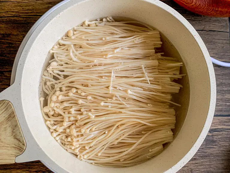 Enoki mushrooms boiling in a white pot until just tender.