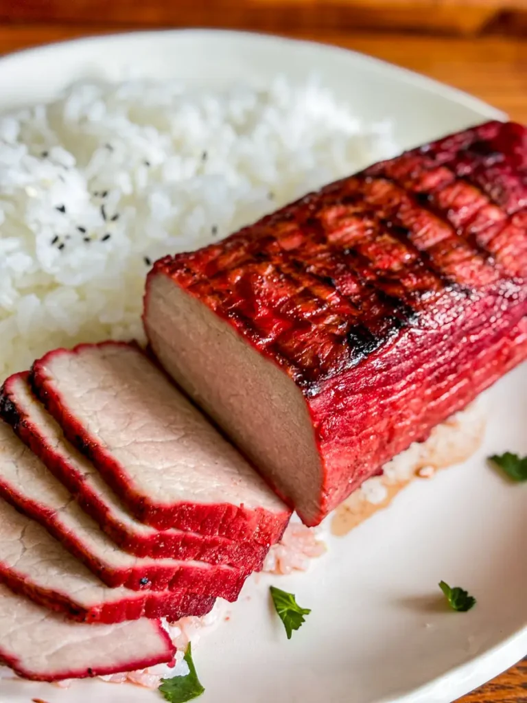 Sliced Chinese char siu pork with a red barbecue crust served over white rice on a white plate.