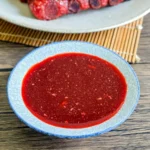 Close-up of homemade red char siu sauce in a small blue bowl on a wooden table.