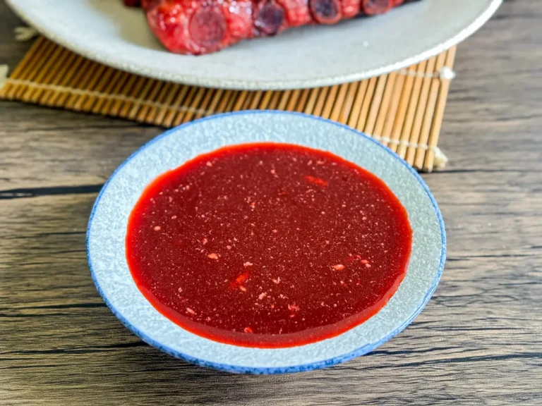 Close-up of homemade red char siu sauce in a small blue bowl on a wooden table.