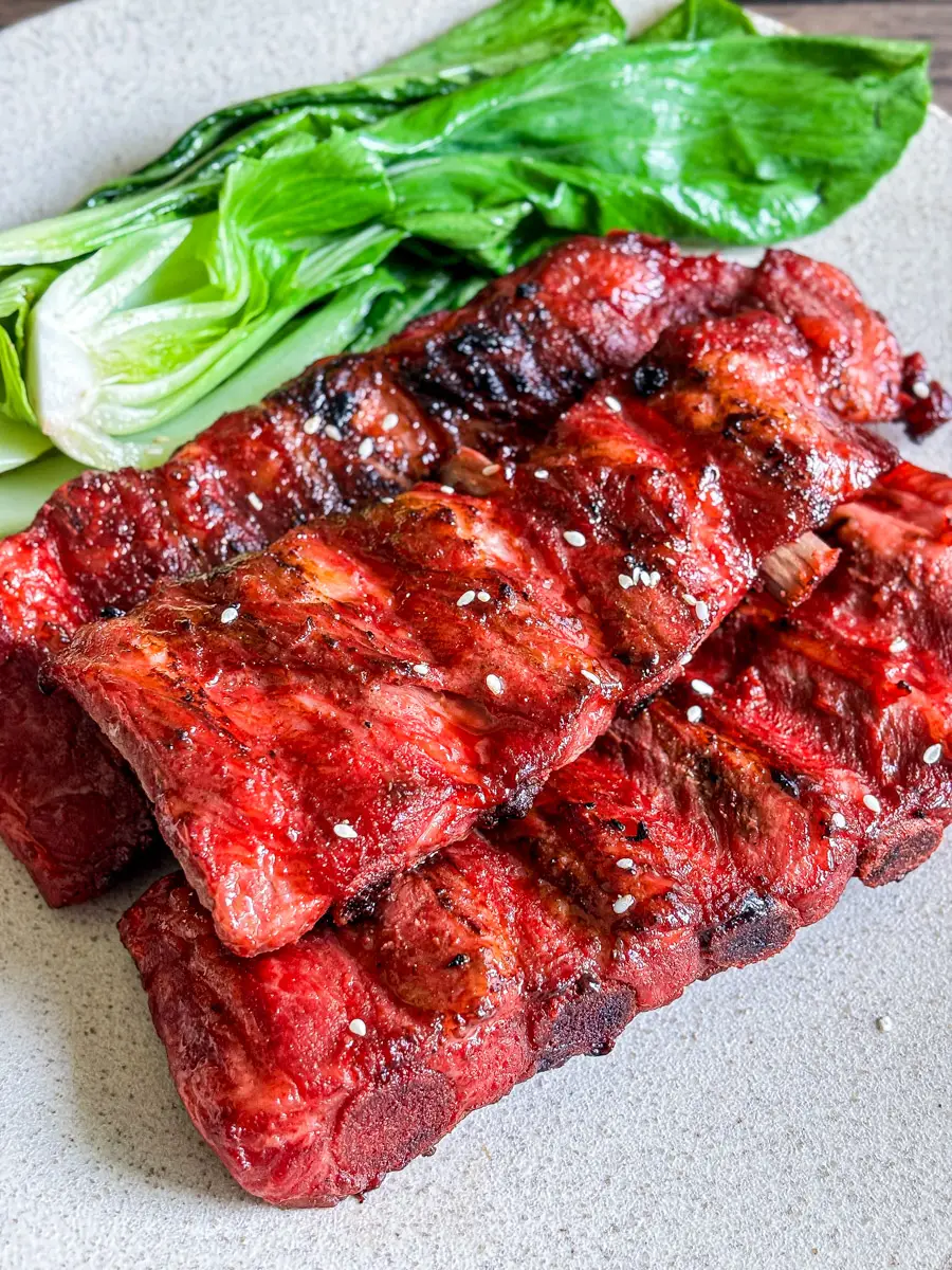 Grilled Chinese BBQ pork ribs with a glossy red char siu glaze, served on a plate with steamed bok choy.