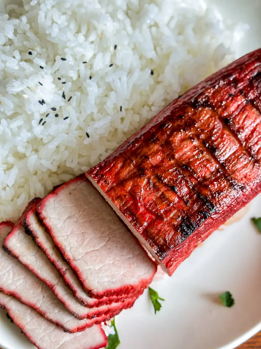 Sliced Chinese BBQ pork tenderloin served with jasmine rice, showing the red caramelized edges and juicy center.
