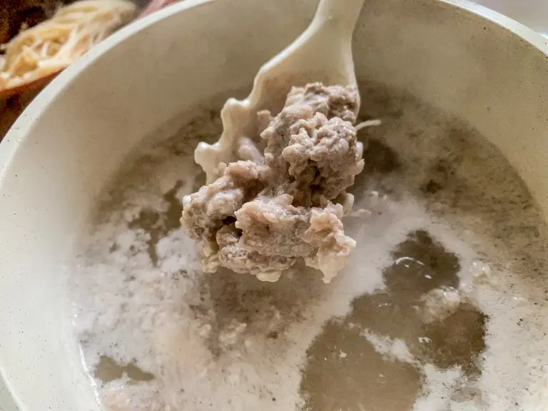 Ground pork simmering in hot water until fully cooked.