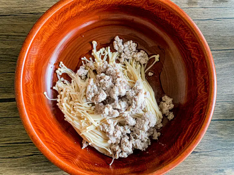 Cooked enoki mushrooms and ground pork combined in a salad bowl.