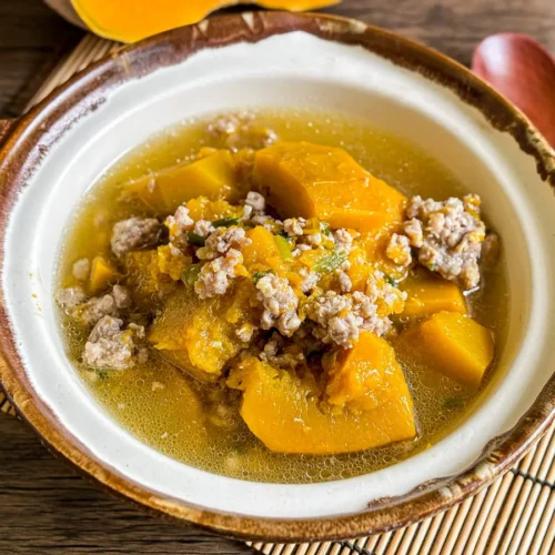 Vietnamese pumpkin soup (canh bi do) – golden pumpkin pieces and minced pork in a light, clear broth in rustic clay bowl.